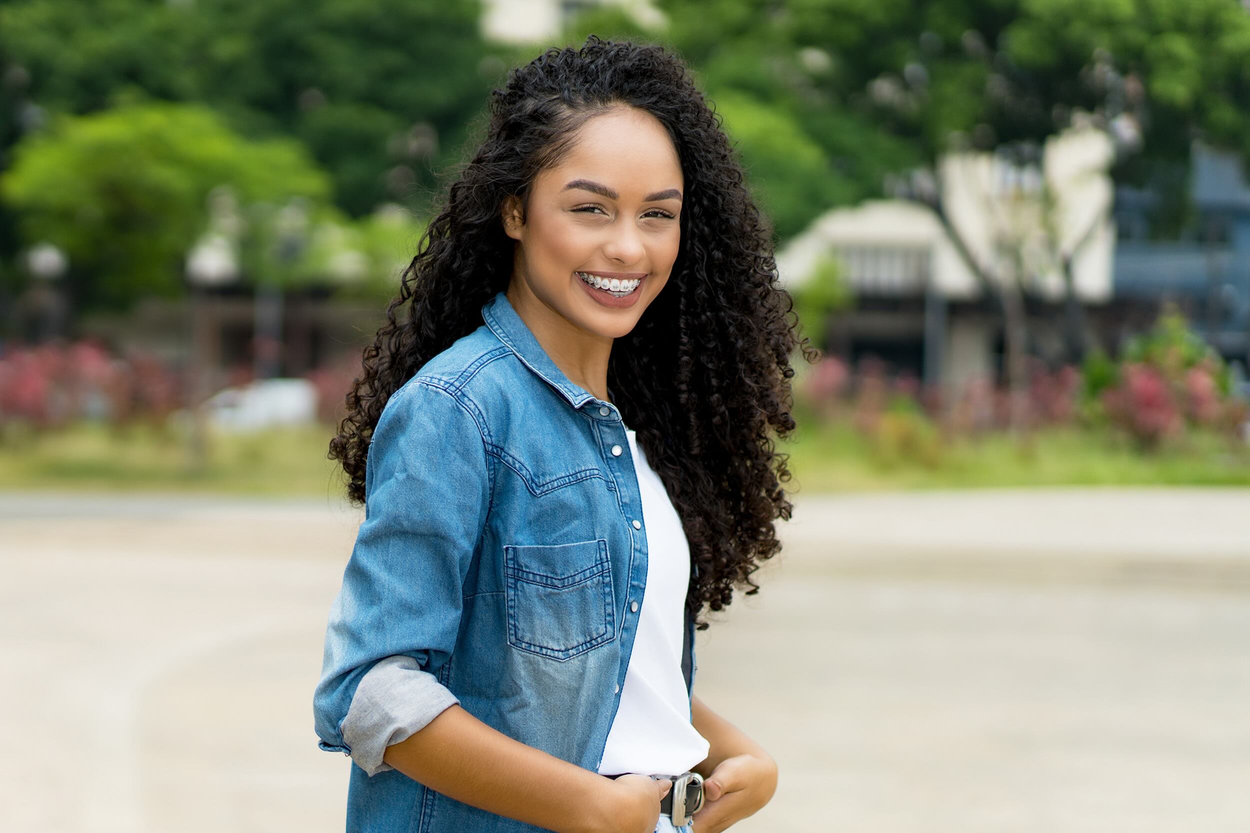 A young woman smiling in a white shirt and denim jacket, showcasing confidence in her orthodontic treatment.