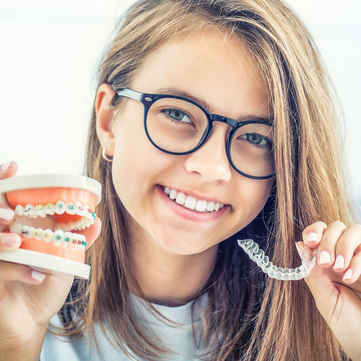 Girl holding braces model and Invisalign tray for orthodontics comparison