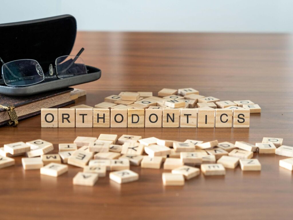 Scrabble tiles spelling "orthodontics" on a wood desk, highlighting dental care and treatments.