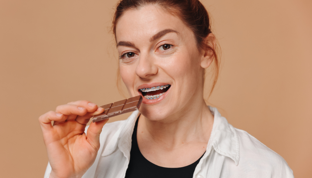 Woman with braces about to eat a chocolate bar, featured in the Valentine's Day treats blog for braces wearers.