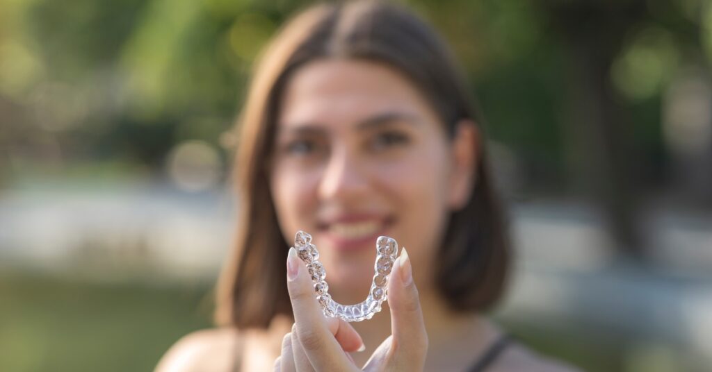 Close-up of Invisalign clear aligners held by a woman, emphasizing their discreet design for busy professionals.