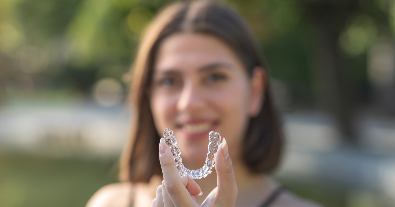 Close-up of Invisalign clear aligners held by a woman, emphasizing their discreet design for busy professionals.