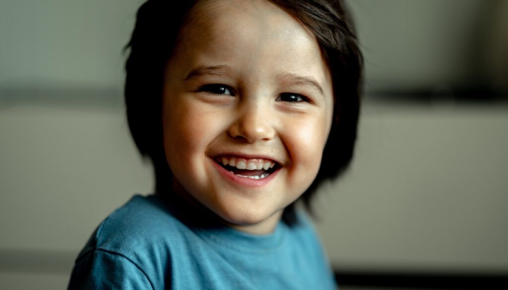 Smiling boy in a blue shirt looking at the camera, representing early orthodontic treatment benefits.