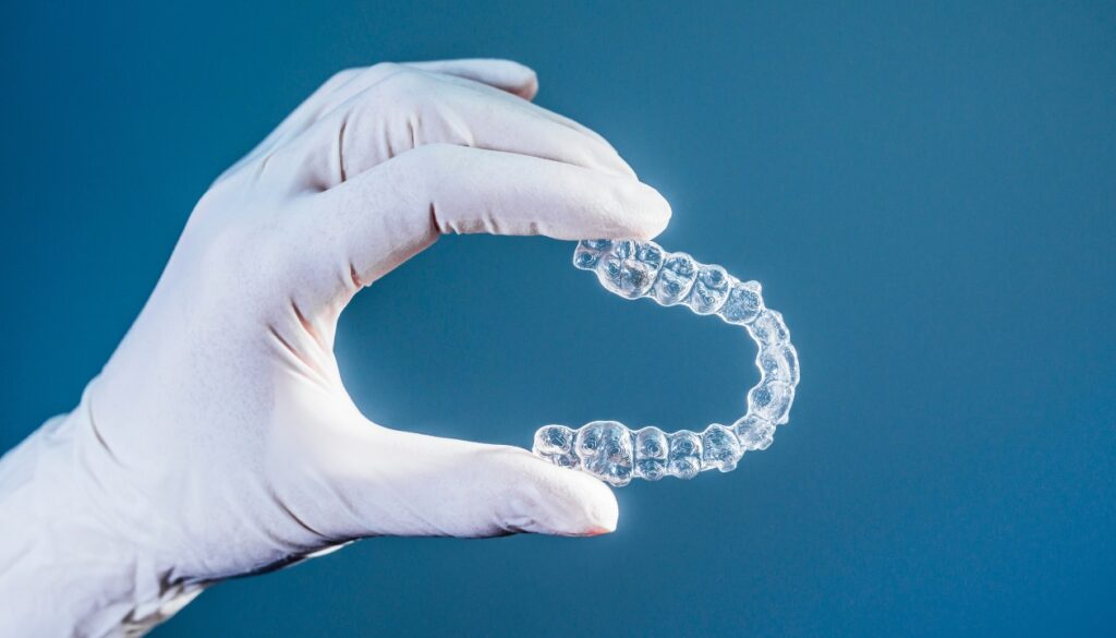 Orthodontist's hand in surgical gloves holding clear aligners by Invisalign, featured in treatment guide blog.
