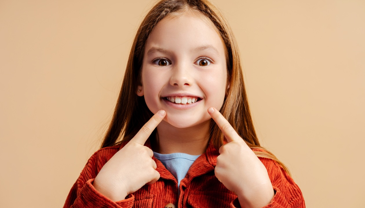 Young girl pointing at her teeth, featured in the blog post on saving time and money with children's orthodontics.