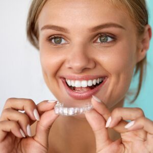 Smiling woman holding clear Invisalign aligner for orthodontic treatment.