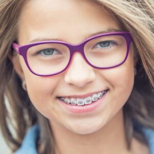 Smiling girl with glasses and braces, representing teen orthodontic care.