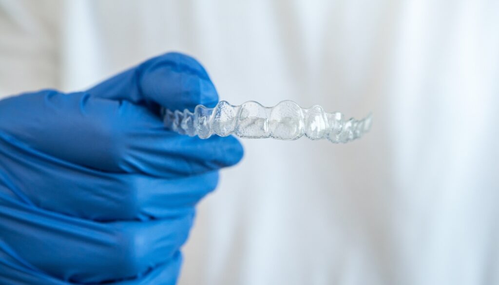 Orthodontist holding clear aligners with blue gloves, featured in the Invisalign guide on Gavri Orthodontics' website.